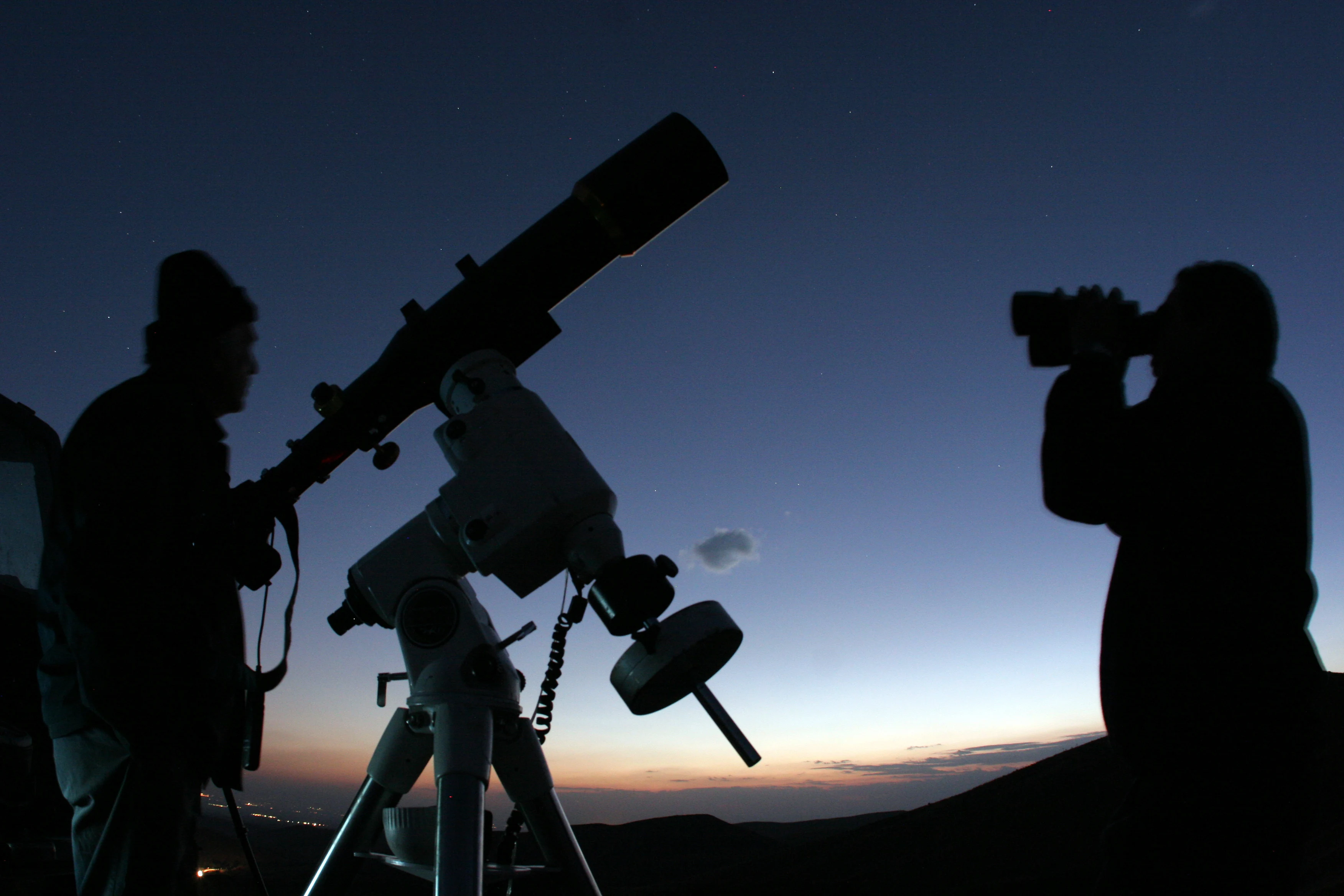 Amateur astronomers preparing telescopes under a starry night sky