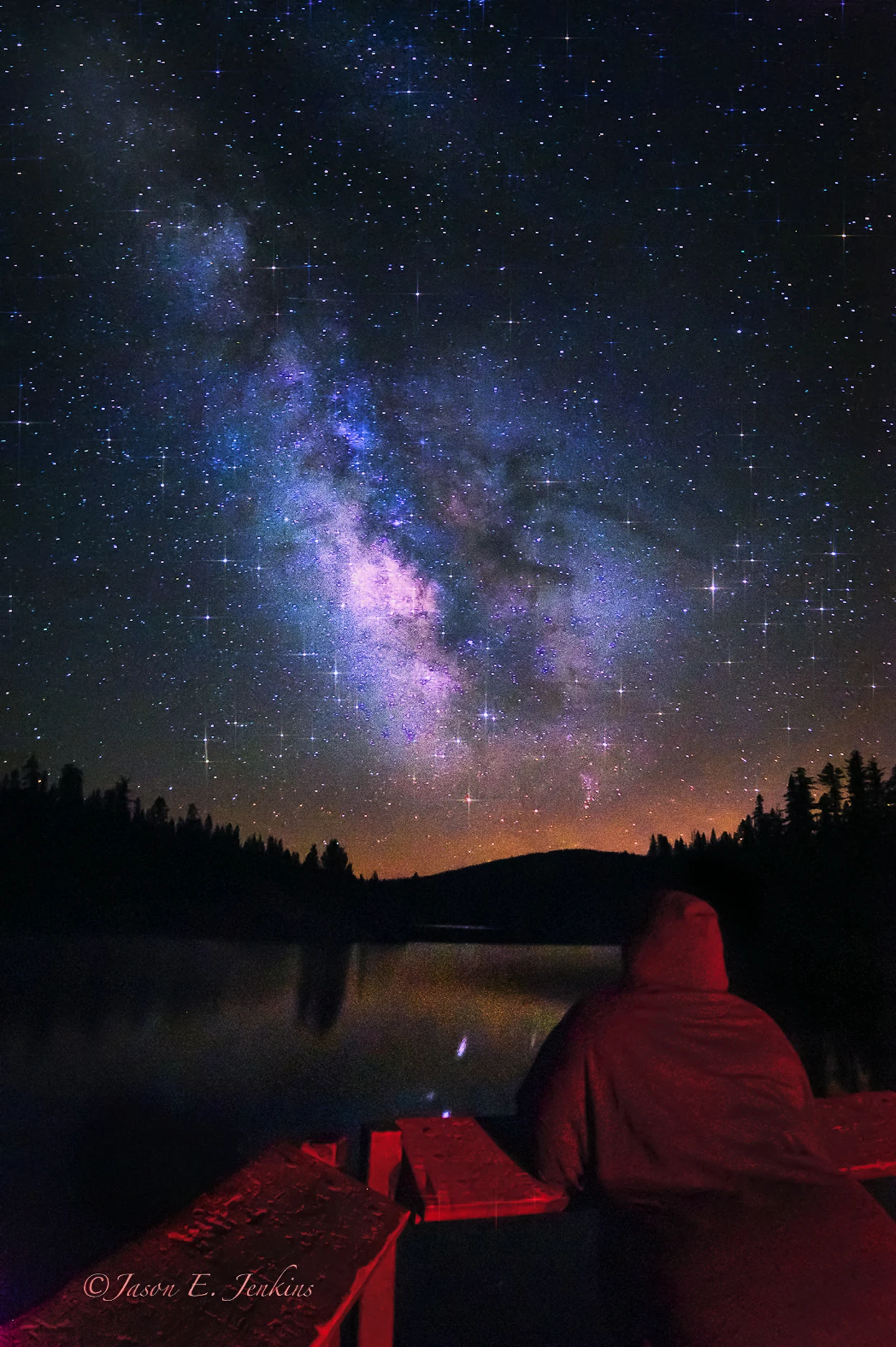 A person gazing at the Milky Way from a mountain lake under a dark sky
