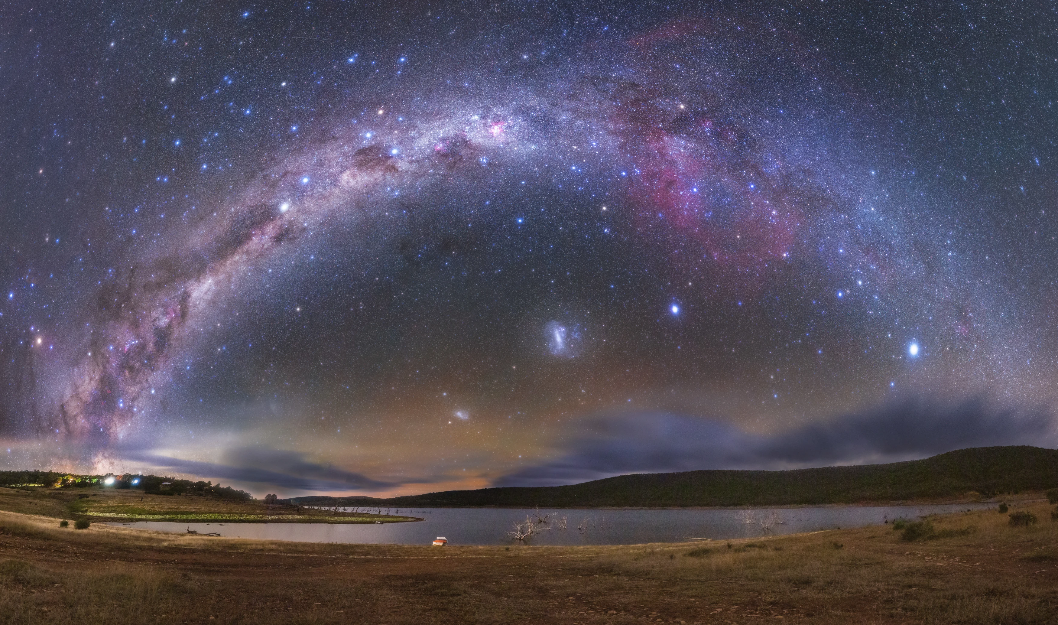 The Milky Way arching over a dark southern hemisphere landscape with the Southern Cross, pointer stars, and Magellanic Clouds visible