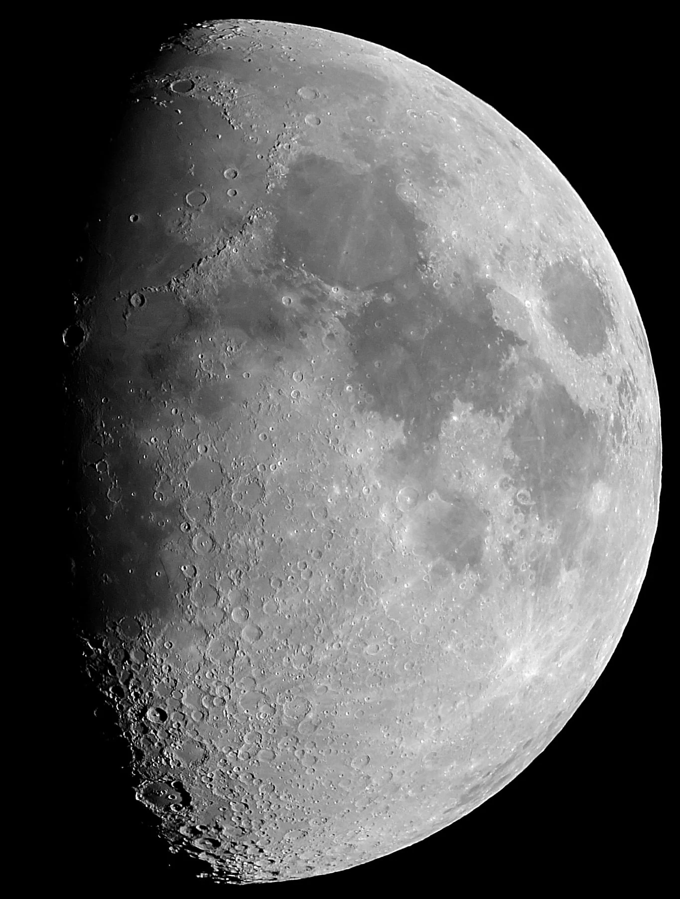 A waxing gibbous Moon through a telescope, craters and mountains thrown into sharp relief along the terminator, the day–night line running down the left of the disc.