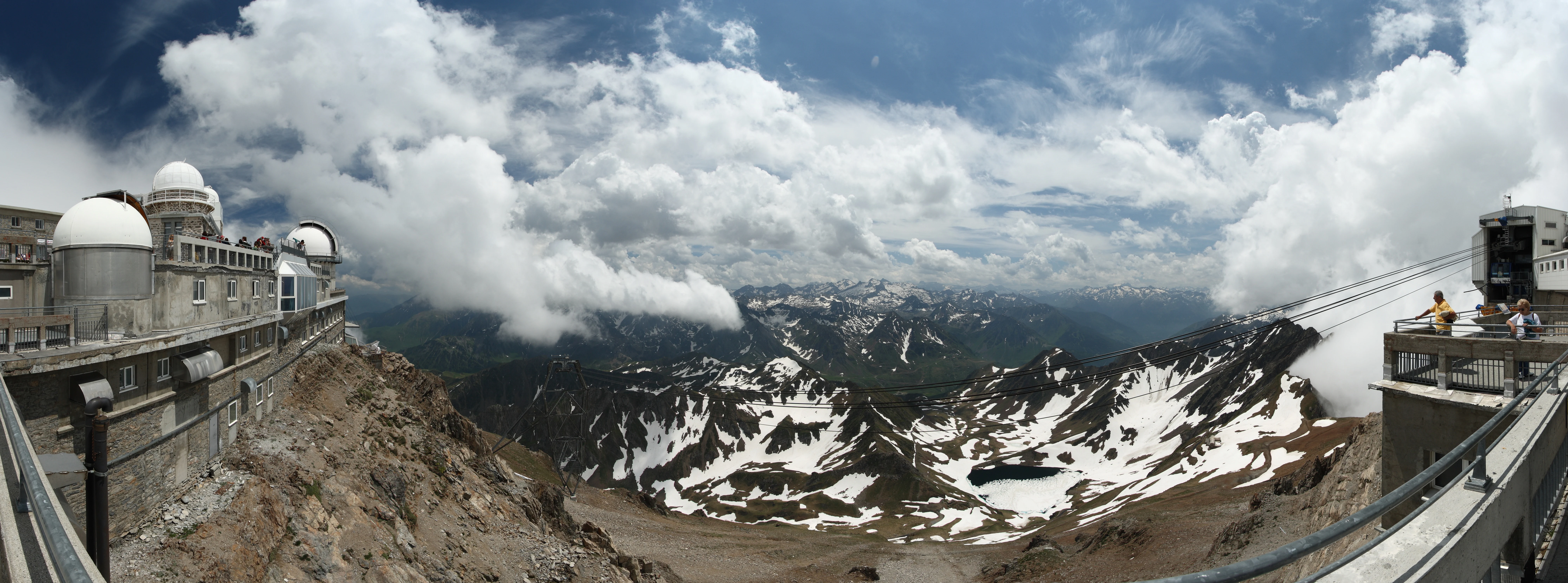 The Pic du Midi de Bigorre observatory domes and summit terraces at 2,877 m, with the cable car cables at right and a snow-streaked Pyrenees panorama beyond.