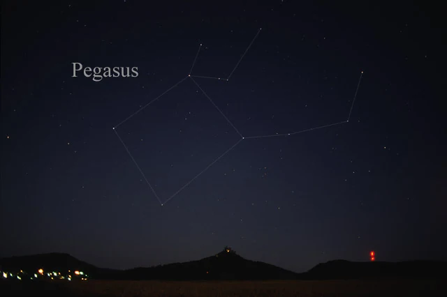 The constellation Pegasus over a dark horizon at night, its four Great Square stars and the horse's neck joined by faint drawn lines and labelled 'Pegasus', with a hilltop silhouette and distant town lights below