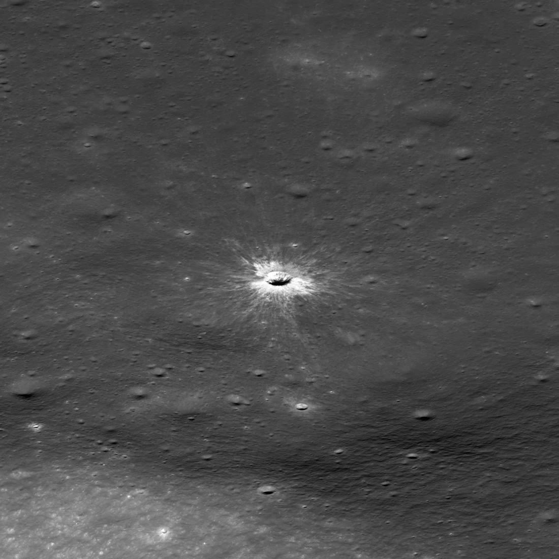 Oblique Lunar Reconnaissance Orbiter view of McGetchin crater, a fresh 222-metre crater on grey lunar plains surrounded by a bright starburst of ejecta rays