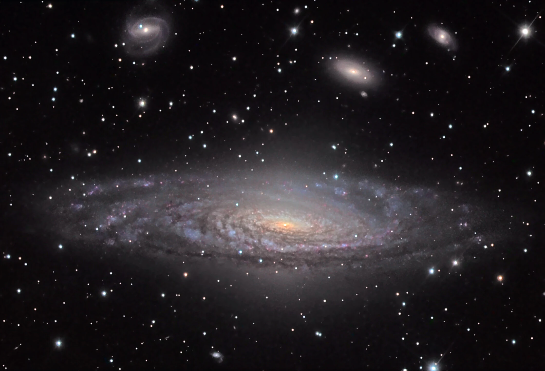 The tilted spiral galaxy NGC 7331 with a golden central bulge, blue-white spiral arms and dark dust lanes, three smaller background galaxies scattered across the star field above it
