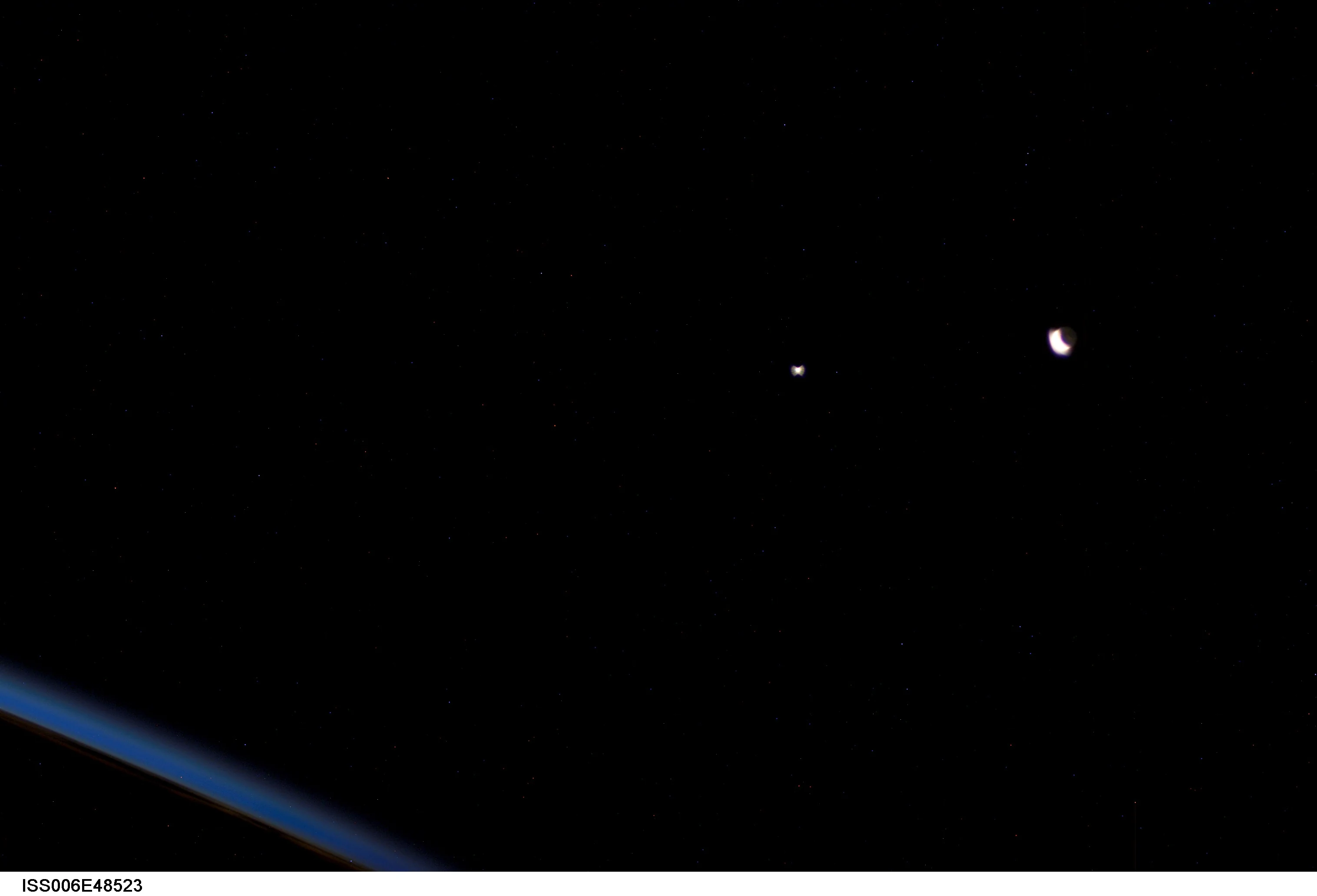 A crescent Moon with faint earthshine at right, the overexposed point of Venus at center, and Earth's blue atmospheric limb at lower left, photographed from the ISS