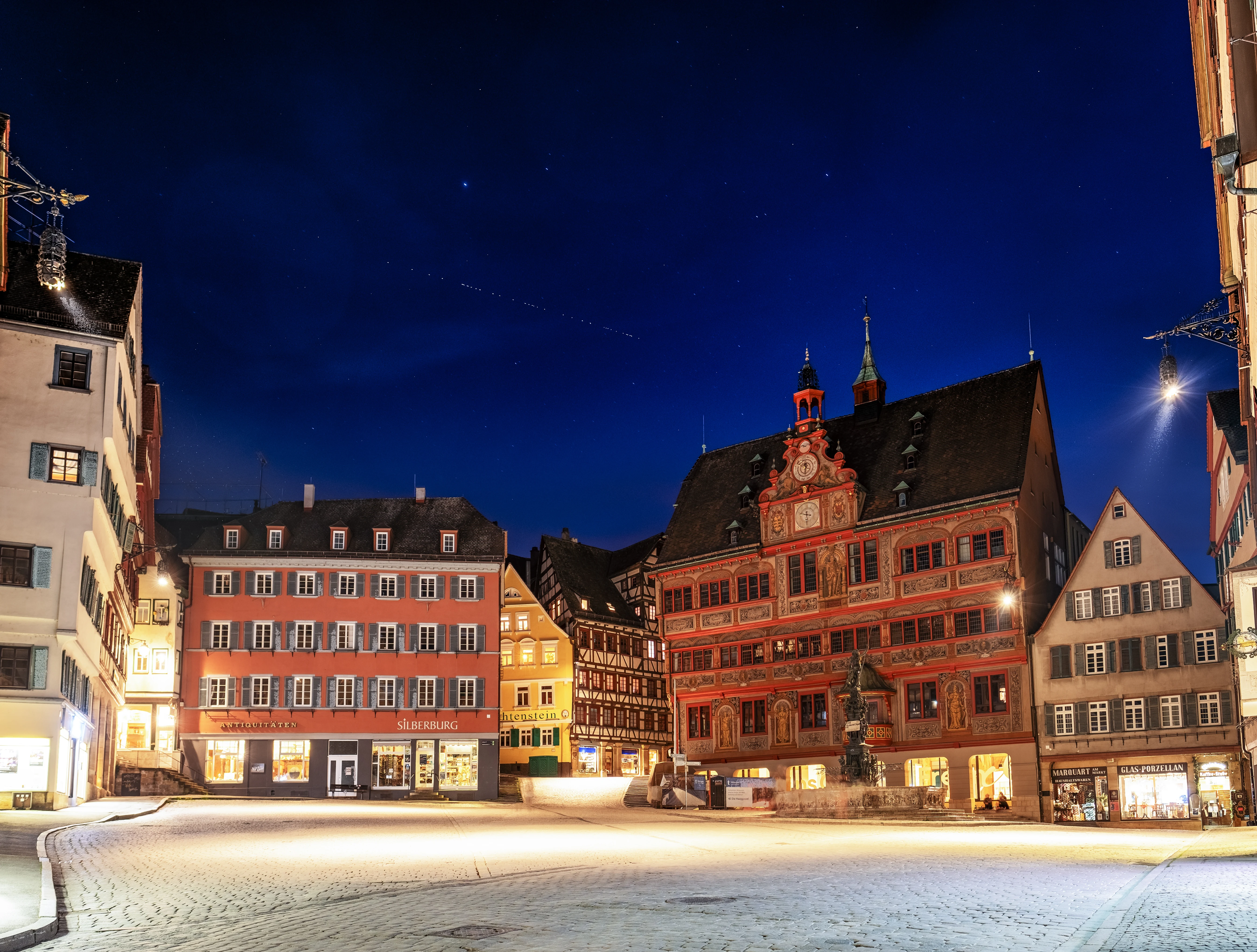 A line of evenly spaced Starlink satellites crossing a deep-blue twilight sky above the painted town hall on Tübingen's market square